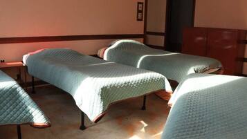 A room with three beds arranged in a row, a wooden cabinet, and a wall-mounted light switch.