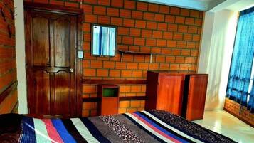 A room with a brick wall, a wooden door, a bed with a striped blanket, and a window with curtains.