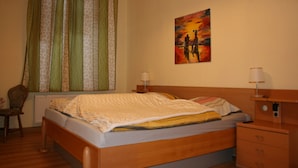 Un dormitorio con una cama, una silla, una mesita de noche, una lámpara y un cuadro en la pared.