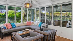 A covered outdoor seating area with a sectional sofa, cushioned chairs, and a hanging light fixture.