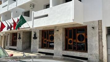 Un edificio de varios pisos con paredes exteriores blancas y balcones. Se observan varias banderas afuera, incluyendo una verde con un emblema blanco.