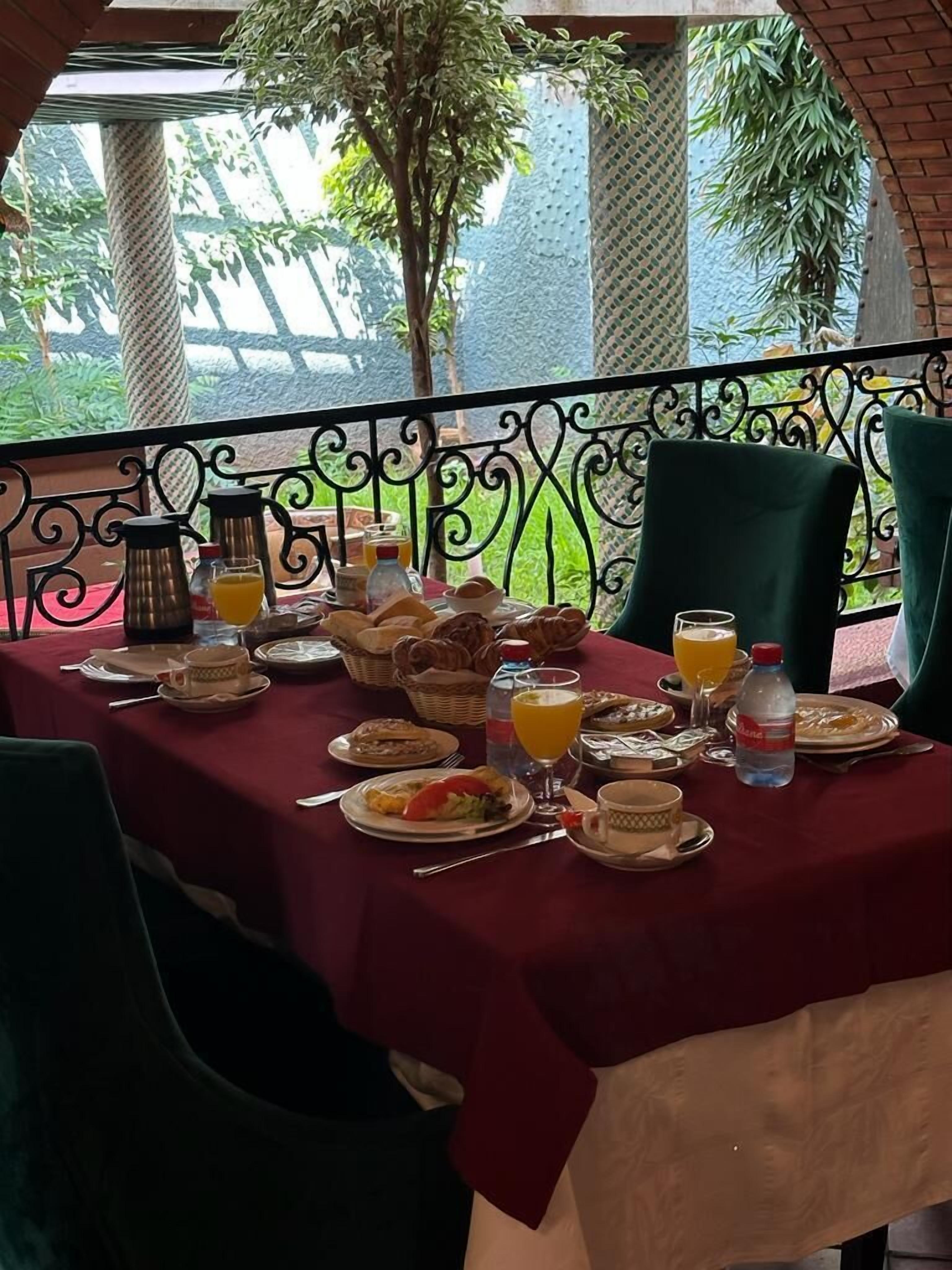 Ein Esstisch ist reichhaltig mit Frühstücksleckereien, darunter Gebäck, Obst und Getränke, gedeckt, und bietet einen Blick auf grüne Natur.