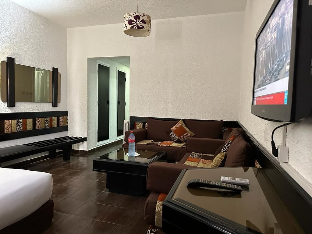 Una habitación de hotel con cama, sofá, mesa de centro, televisor y un banco.