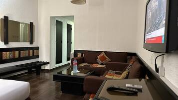 Una habitación de hotel con cama, sofá, mesa de centro, televisor y un banco.