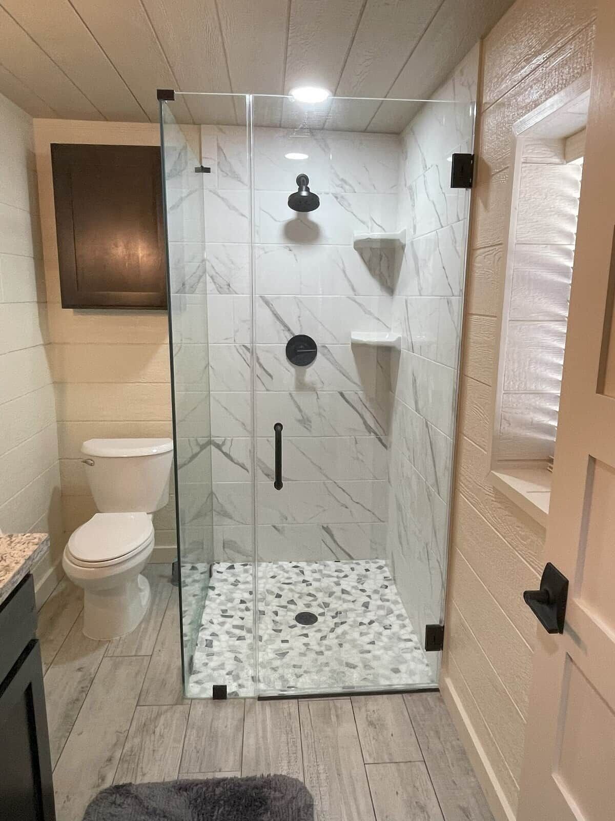 Un baño con ducha de vidrio, inodoro y suelo estampado con diseño de mármol.