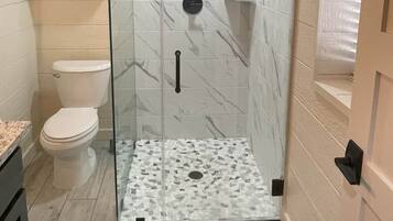 Un baño con ducha de vidrio, inodoro y suelo estampado con diseño de mármol.
