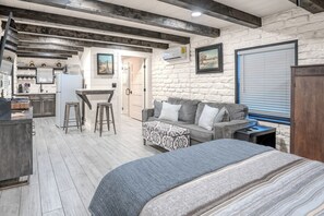 A room with a bed, a sofa, a kitchen area, and a stone wall.