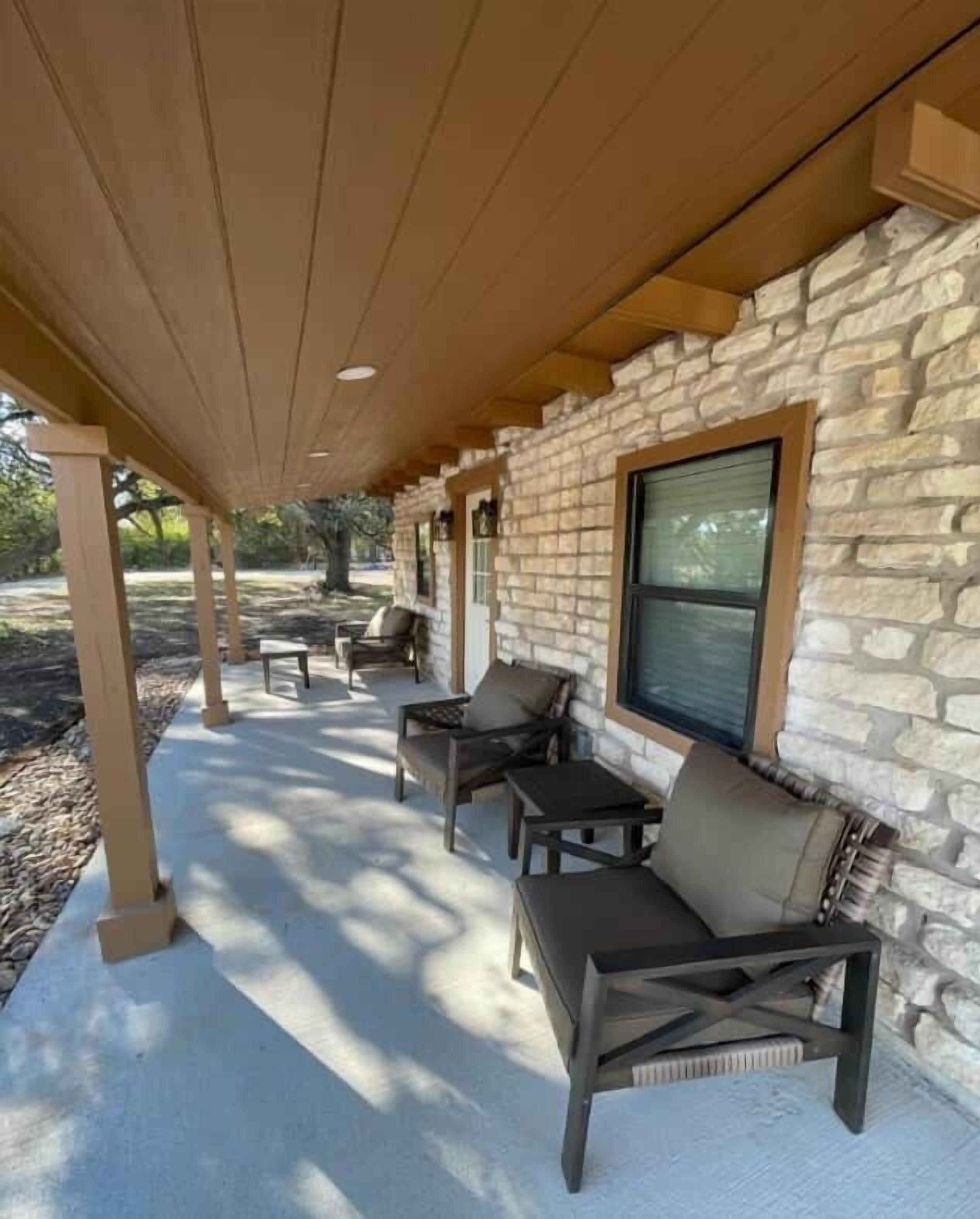 A covered patio area with stone walls, outdoor furniture, and a window.