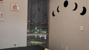 Un dormitorio con cama, ventana con persianas y decoración de luna creciente en la pared.