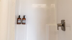 A bathroom with a shower, a white door, and two bottles of shampoo on a shelf. - Casita Inn #5 - Queen (Wayne County)