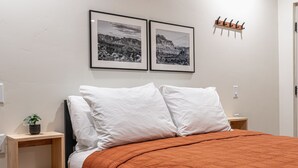 A bedroom with a bed, two pillows, a nightstand with a plant, and two framed pictures on the wall. - Casita Inn #5 - Queen (Wayne County)