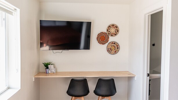 A room with a TV mounted on the wall, a wooden shelf below, two black chairs, and three decorative plates. - Casita Inn #5 - Queen (Wayne County)