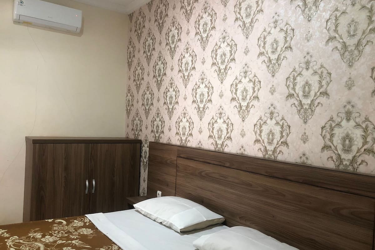 A bedroom with a wooden headboard, a bed with white bedding, and a patterned wallpaper.