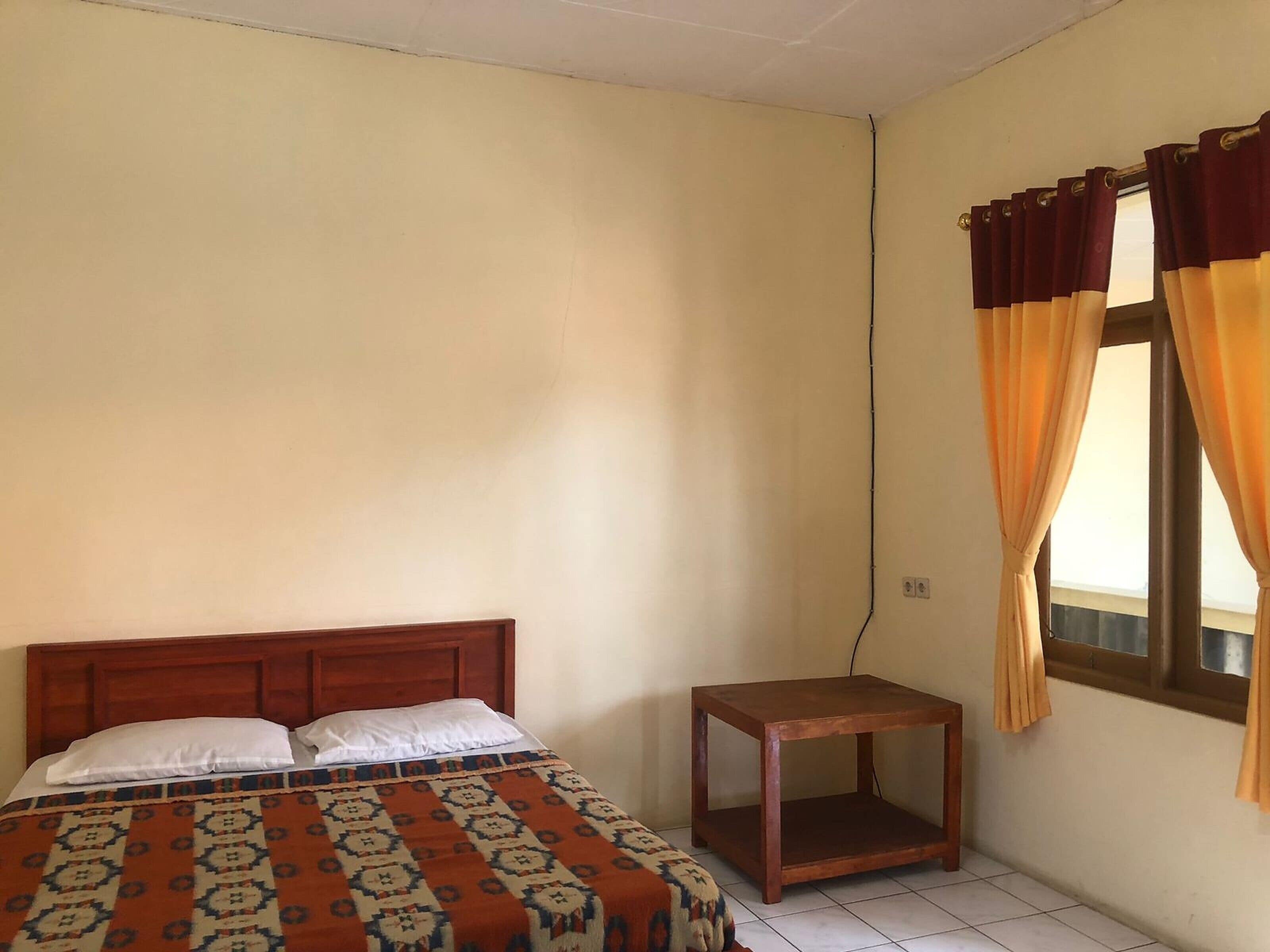 A bedroom with a bed, a small wooden nightstand, and a window with curtains.