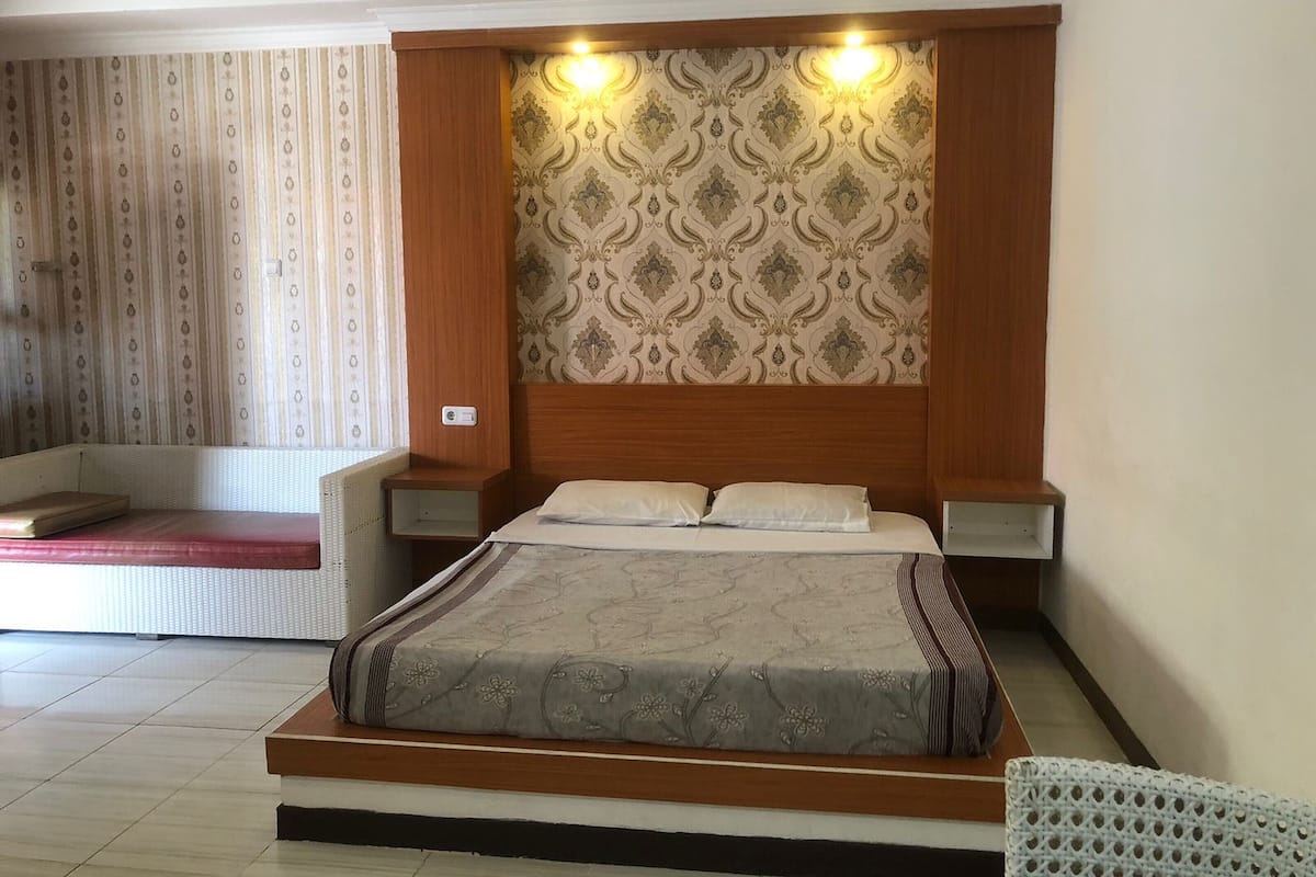 A bedroom with a large bed, wooden headboard, two bedside tables, and a patterned wallpaper.
