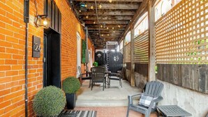 Een gebouw van baksteen met een bord met het nummer '26', terras met stoelen en tafels, en een houten plafond met zichtbare balken.