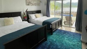 Une chambre d’hôtel avec deux lits, un ventilateur de plafond, une grande fenêtre donnant sur l’extérieur et une porte-fenêtre coulissante qui mène à un balcon.
