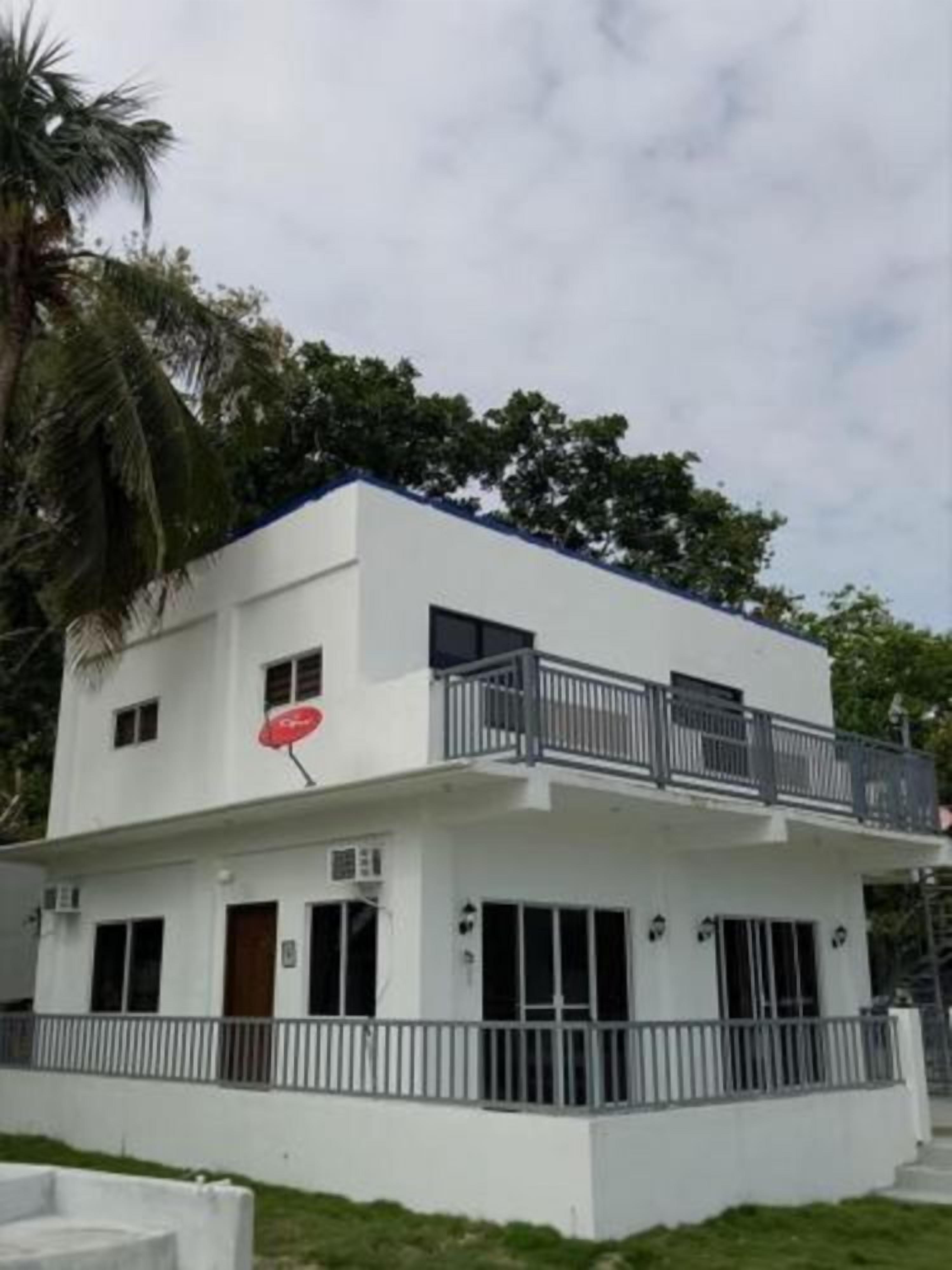 Un bâtiment à deux étages, à l’extérieur blanc, avec un balcon au dernier étage et une antenne parabolique sur le côté.