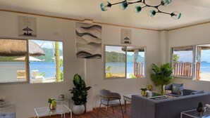 Un salon spacieux avec une grande fenêtre donnant sur une plage, un canapé, une table basse et un fauteuil.