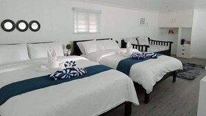 Una camera d'albergo con due letti, una piccola finestra, un armadio bianco e uno specchio a parete.