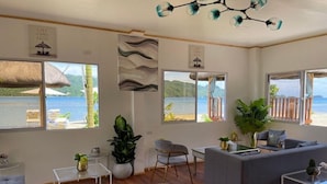 A spacious living room with a large window overlooking a beach, a sofa, a coffee table, and a chair. - Beautiful Junior Suite in Lopez Beach Resort (Sipalay, Negros Occidental)