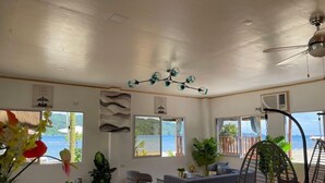 Un amplio espacio de sala con un ventanal que ofrece vistas al mar, un ventilador de techo y un sillón colgante.