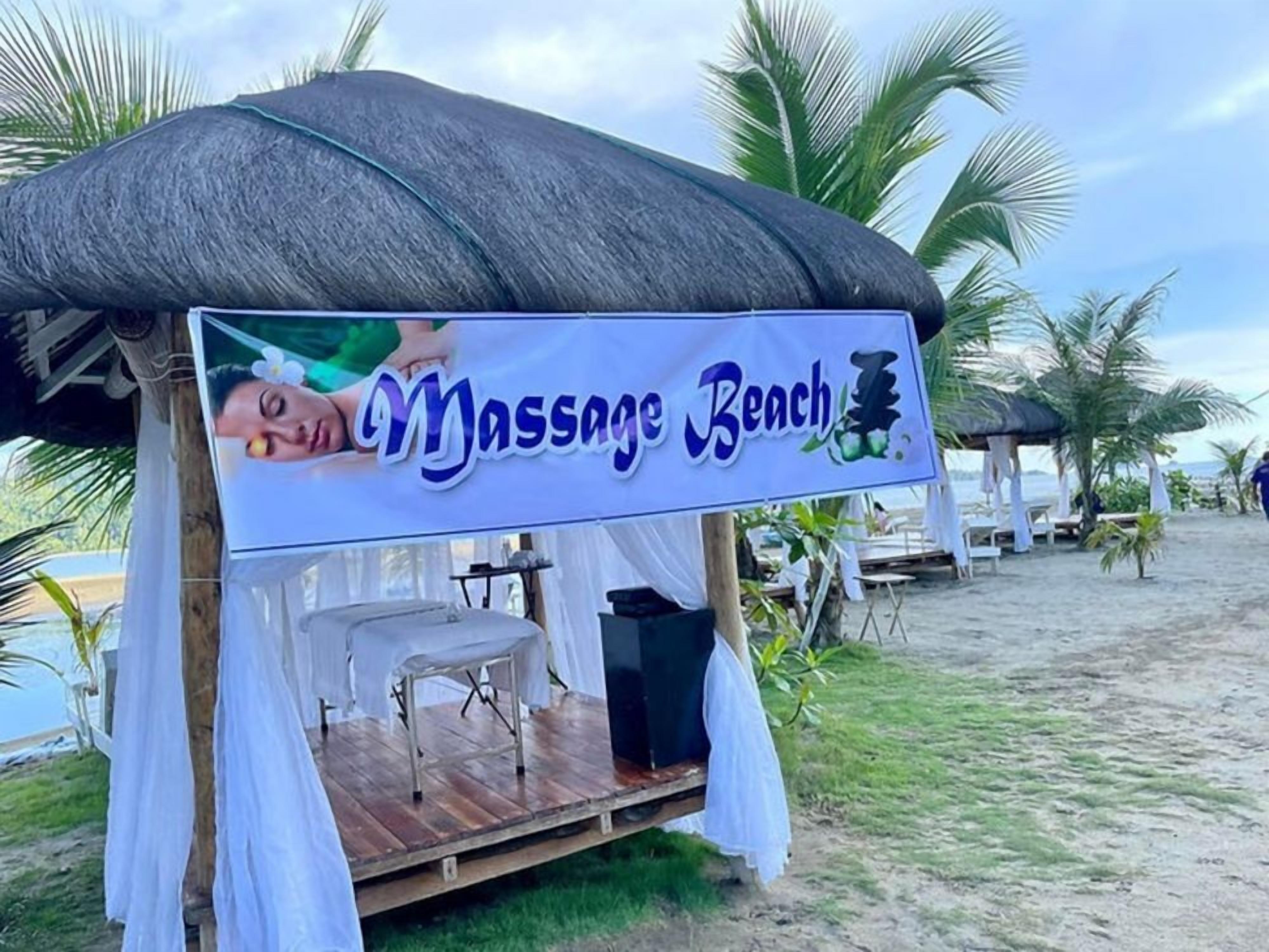 A massage tent with a sign reading "Massage Beach" on a beach with palm trees.