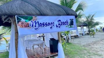 A massage tent with a sign reading "Massage Beach" on a beach with palm trees.