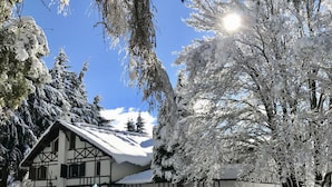 Una cabaña tradicional con techo inclinado, rodeada de árboles cubiertos de nieve y un cielo azul despejado.