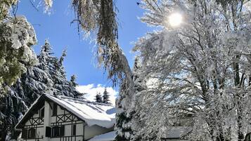 Um chalé tradicional com telhado inclinado, rodeado por árvores cobertas de neve e um céu azul claro.