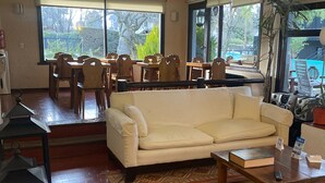 Amplia sala de estar con un sofá beige, una mesa de centro de madera y un tapete estampado. Se observa un comedor con sillas de madera y una mesa al fondo.