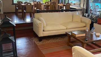 Uma sala de estar espaçosa com um sofá bege, uma mesa de centro de madeira e um tapete estampado. Ao fundo, há uma área de jantar com cadeiras e mesa de madeira.
