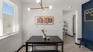 A modern interior with a black dining table, a colorful abstract painting, and a 'Welcome' sign on a blue wall. - King Bed, Fenced Yard, Parking, TV’s in all rooms! Near parks  (Fort Wayne)