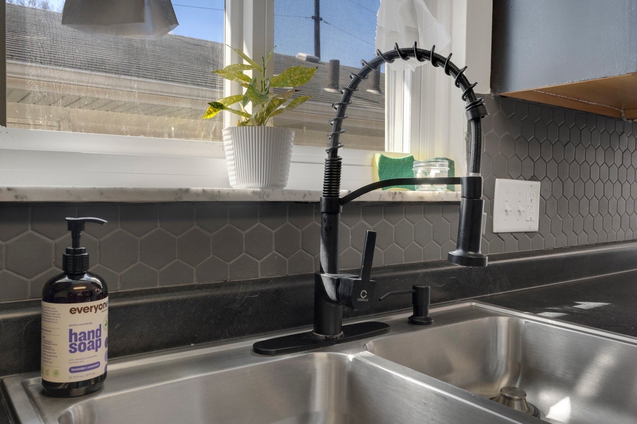 A kitchen with a modern faucet, a potted plant, and a bottle of hand soap on the counter.