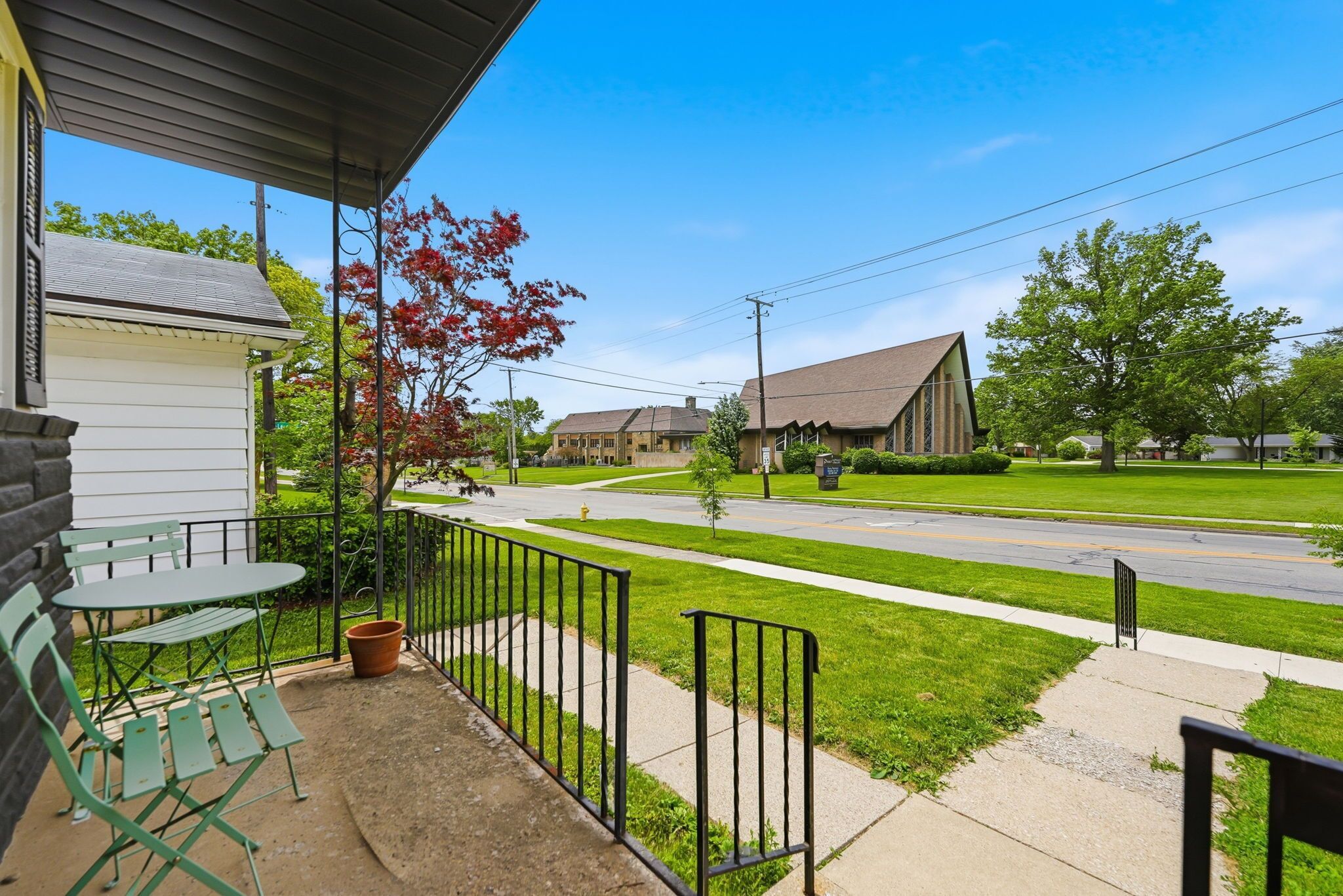 A porch with a table and chairs, a small shed, and a street view with houses and a road.