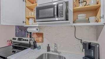 Cocina compacta con microondas integrado, cafetera y pileta de acero inoxidable.