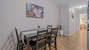 A dining area with a table and chairs, a painting on the wall, and a hallway leading to another room. - Private Apartment on River Ave. close to main st (Patchogue)