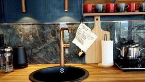 Una cucina con lavello nero, piano di lavoro in legno e schienale in marmo.