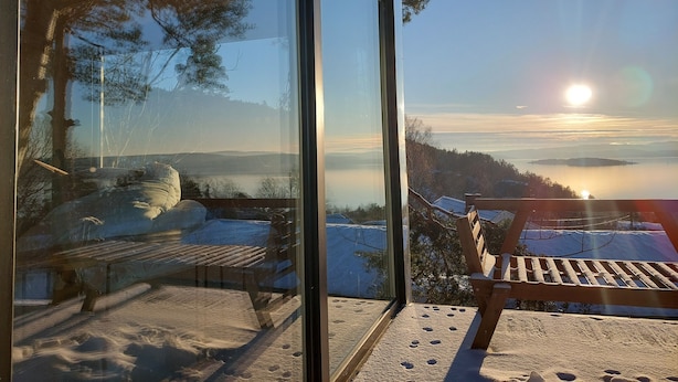 Dalla finestra in vetro, vista panoramica su un paesaggio innevato con una panca e una sedia di legno.