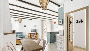 A dining area with a wooden table and pink chairs, a kitchen with teal cabinets, and a living room with a blue sofa. - WELCS APARTAMENTO 102 EMP con Piscina (Empuriabrava)