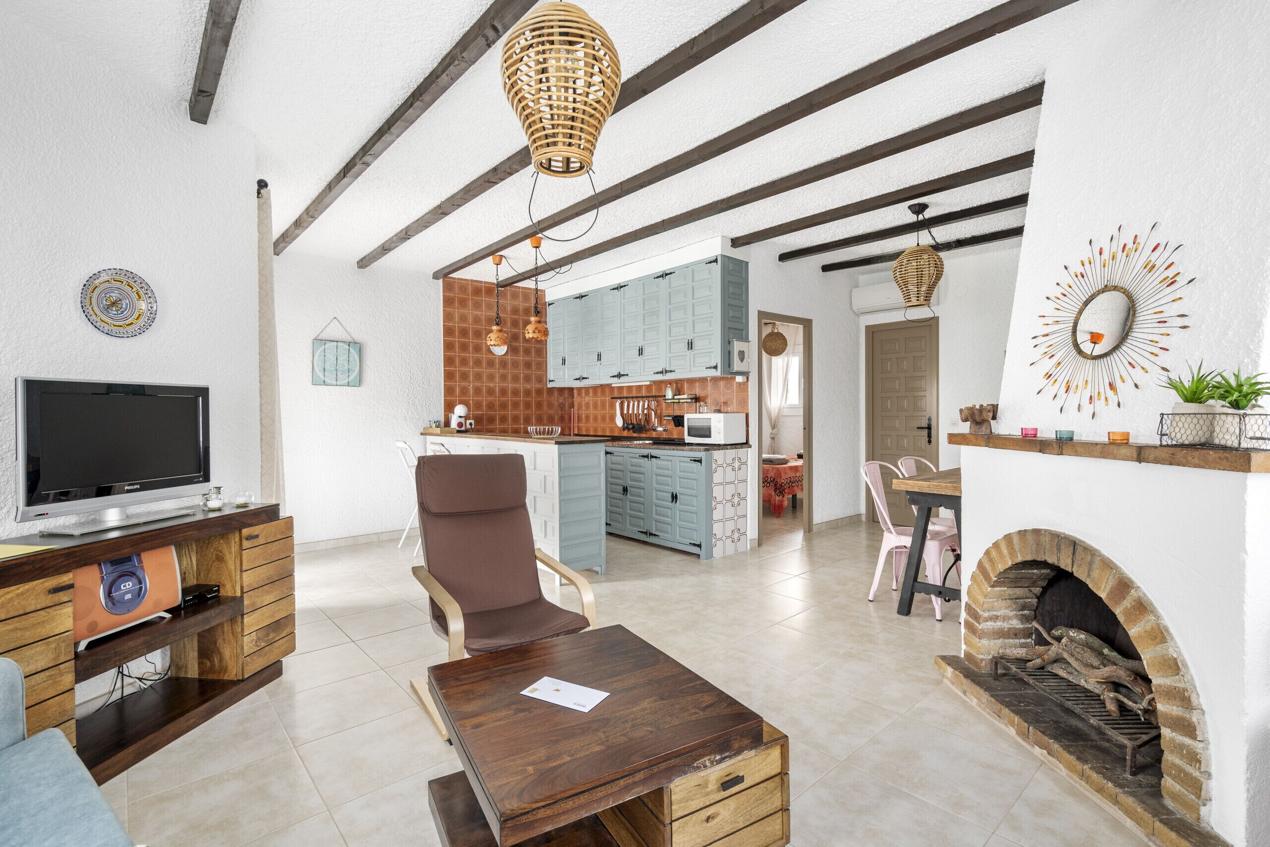 Una sala de estar moderna con televisión, muebles de madera, chimenea y cocina al fondo.