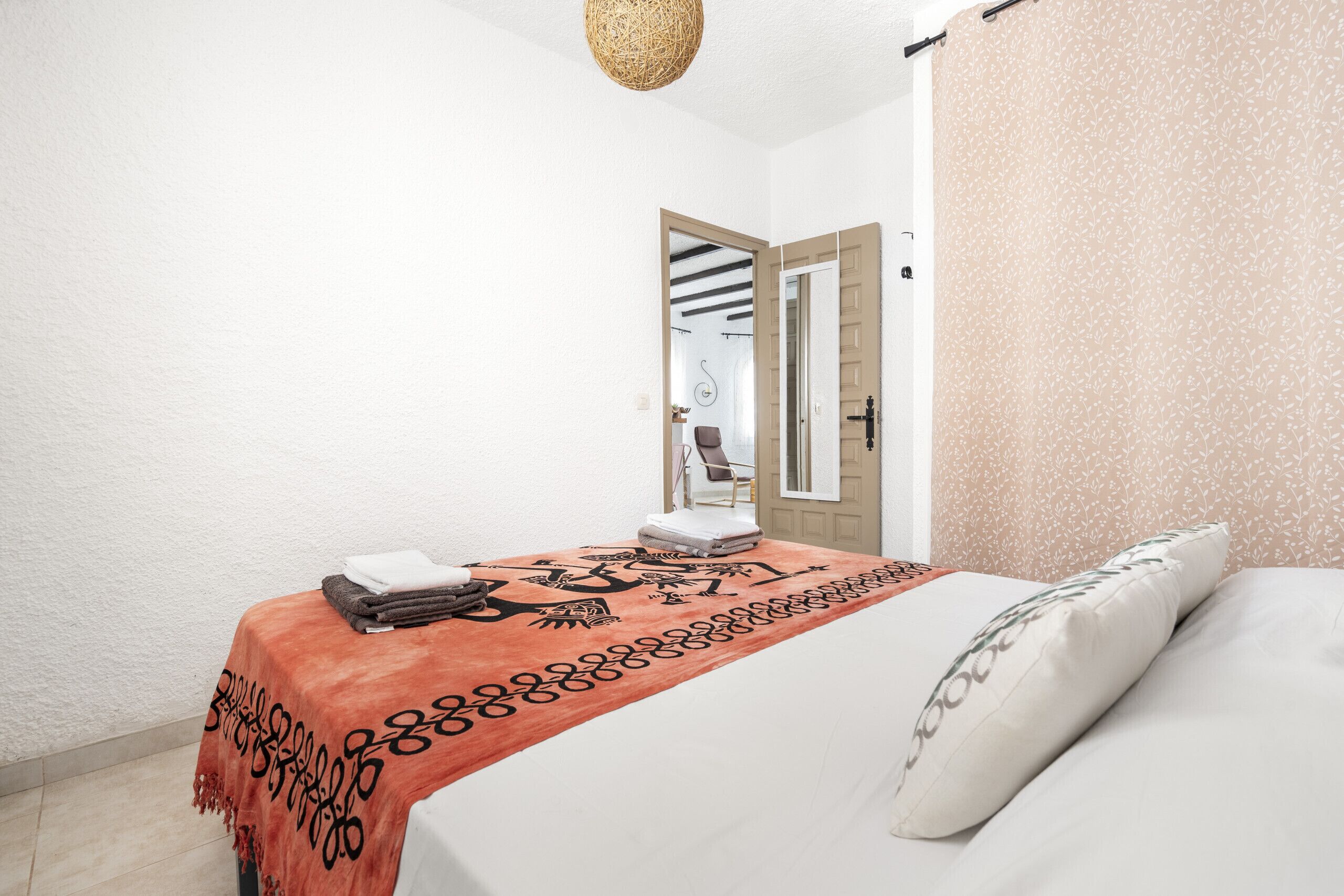 Een slaapkamer met een bed, een tafeltje met een plaid en een deur die naar een andere kamer leidt.