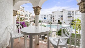A balcony with white chairs and a table, overlooking a pool and residential buildings. - WELCS APARTAMENTO 102 EMP con Piscina (Empuriabrava)