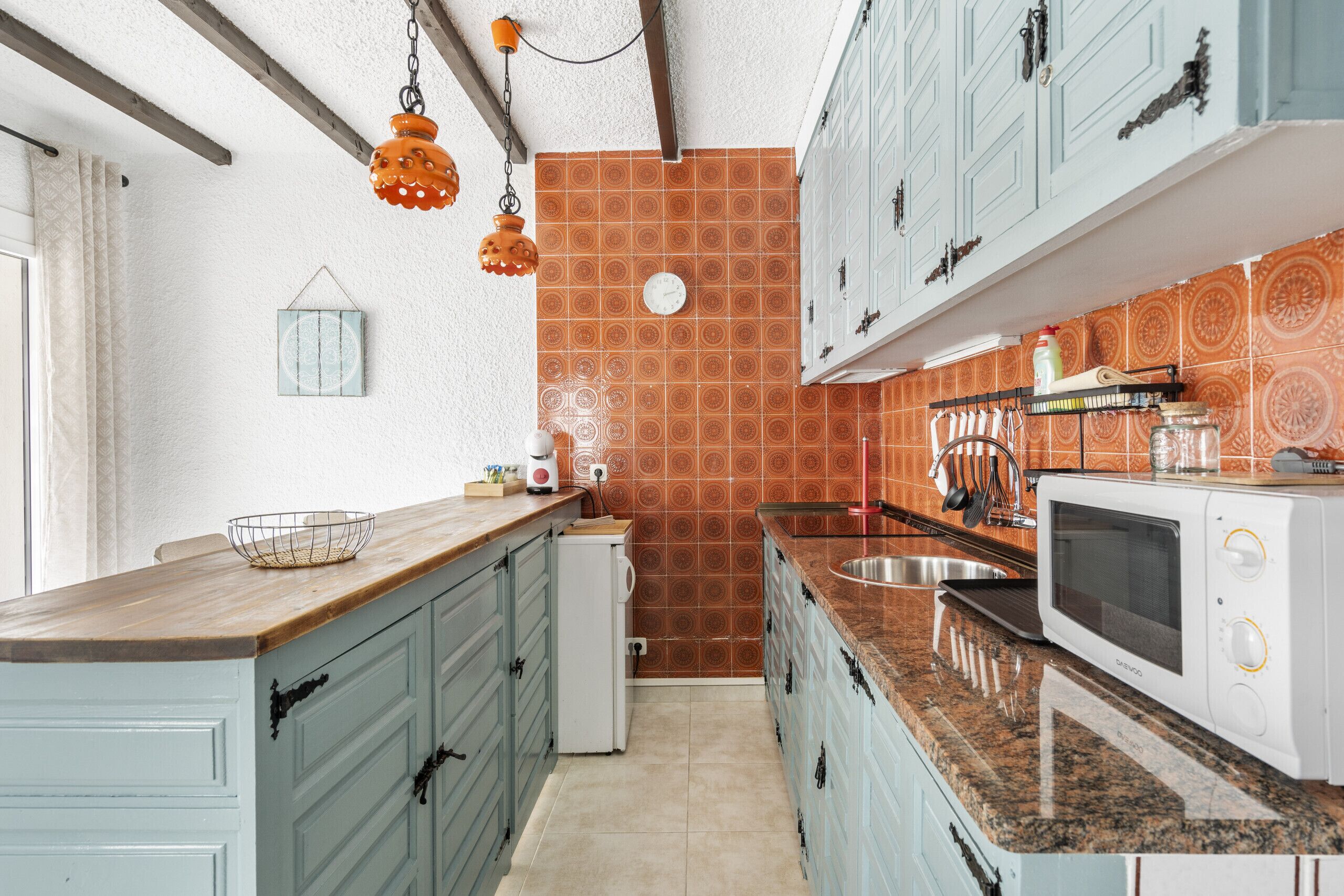 Una cocina con armarios azul verdoso, un microondas y una lámpara colgante naranja.