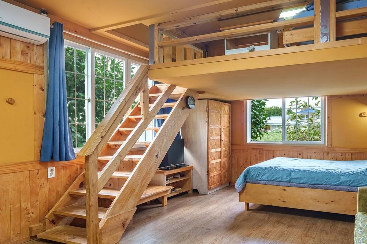 Una habitación con una litera, una escalera de madera y un televisor sobre una estantería.