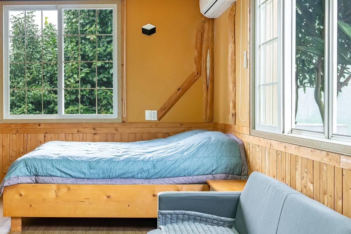 Un dormitorio con cama de madera, una mesita pequeña y una ventana con vistas a la vegetación.