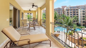 Un balcon avec vue sur la piscine, un coin repas avec des chaises et une table, et un ventilateur de plafond.