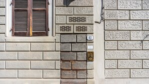 A building facade with a brick wall, a wooden shuttered window, and a door with a brass knocker. - Venezia Double in Firenze (Florence)
