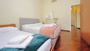 Hotellihuone, jossa on kaksi sänkyä, puulattia, peili ja ovi, joka johtaa toiseen huoneeseen.