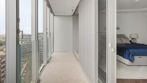 A narrow balcony with a city view, a bedroom with a bed and a nightstand, and a sliding glass door. - Battersea Power Station Flat With River Views (London)